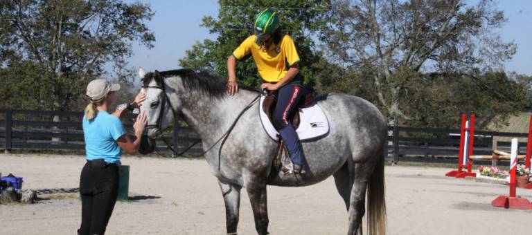 Rider and instructor patting horse during a riding lesson.